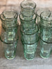 This image displays a collection of recycled glass chai cups, used daily in India for serving chai, water, mint tea, and espresso. The cups, featuring a ribbed texture and a slight green tint, are small and uniform in design, showcasing their stackable quality for easy storage.