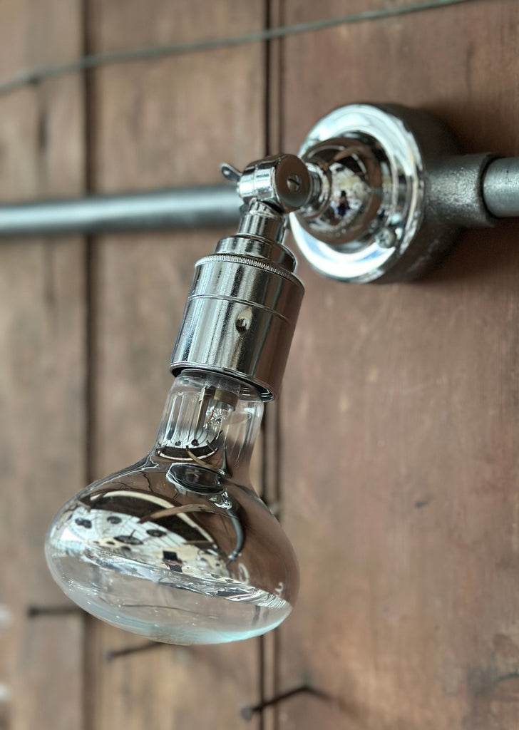 chrome spotlight light fixture comprised of a chrome patress and hinged chrome bulb holder and bulb which allows the light to be positioned in the vertical axis. 