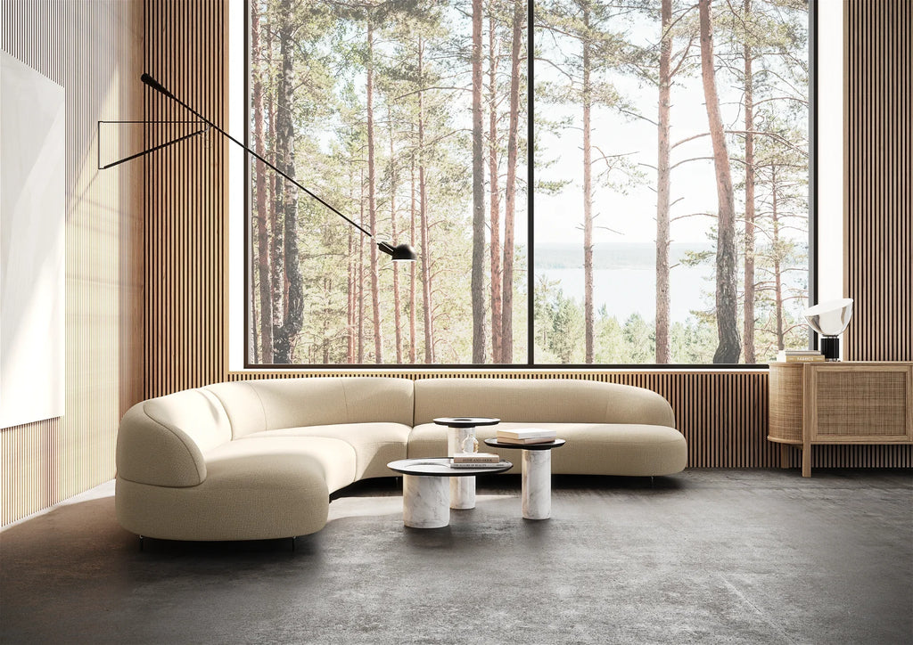 lifestyle photograph of a cream coloured corner sofa in a large modern room with marble coffee tables in front of it. the sofa has soft curves and a low back and appears to float above the ground due to the discrete metal legs