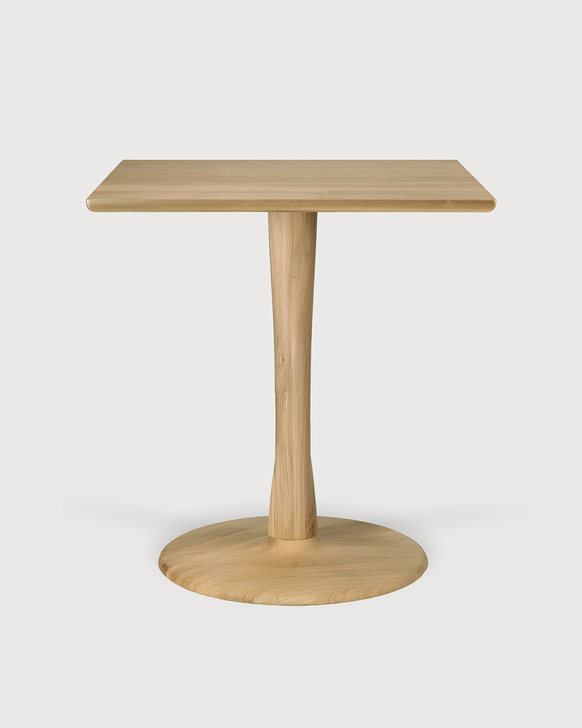 This image features the Lottie Oak Pedestal Table, a stylish and elegant piece suitable for any modern dining area. The table is crafted from solid oak and finished with a matte varnish, emphasizing its natural wood texture and color.