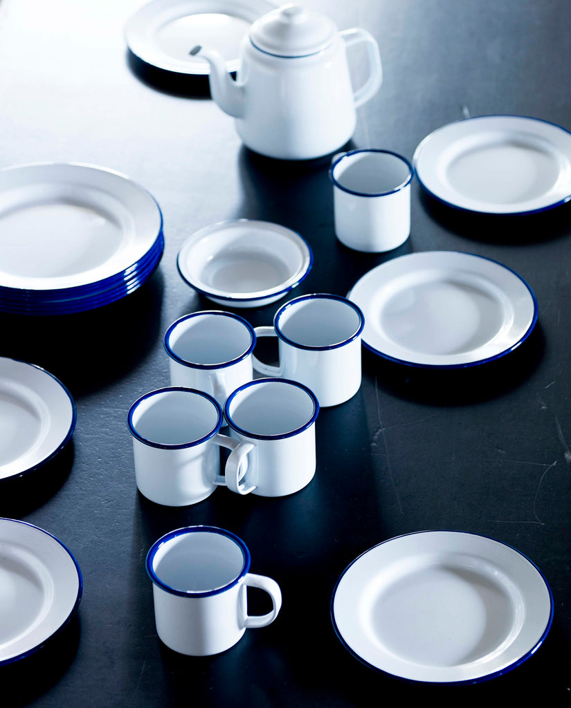 White enamelware plates, mugs, dishes and teapots with blue stripe rims.