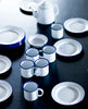 White enamelware plates, mugs, dishes and teapots with blue stripe rims.